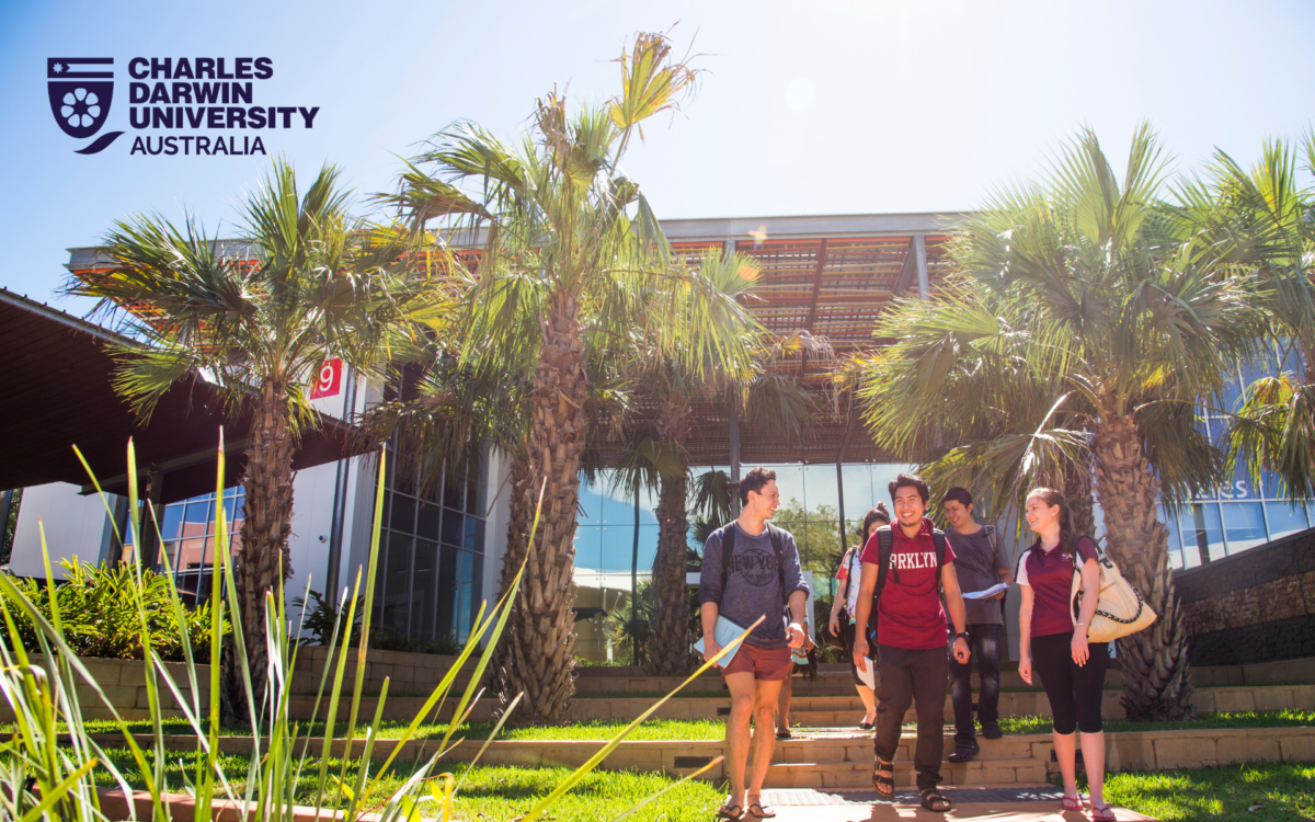 A group of students walks on a sunny day in front of a CDU building at Charles Darwin University, Australia, with the university's logo clearly visible in the top left corner.