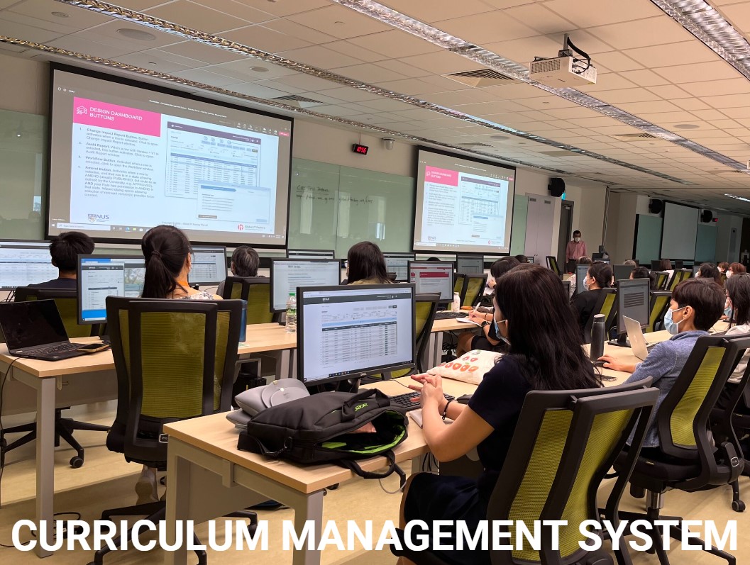 A university classroom with students using laptops and viewing a presentation on a curriculum management system.