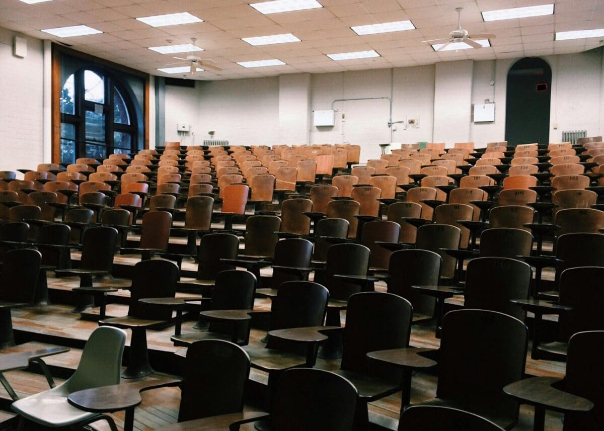 Empty lecture hall with rows of brown chairs facing a whiteboard, arched windows on the back wall, designed for optimal LMS integration.